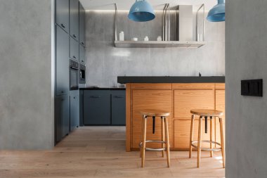 İç dekorasyonlu bir stüdyo daire. Koyu tezgahlı mutfak adası, ahşap bar taburesi, dolap mobilyası ve modern ev aletleri.