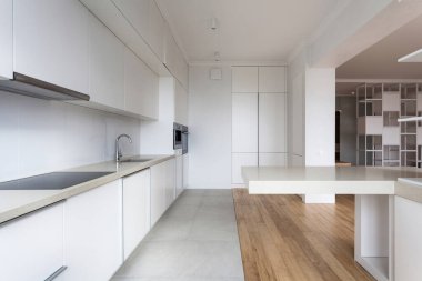 Modern dairede minimalist mutfak. Entegre cihazları olan yeni ve beyaz bir dolap. Boş tezgah masası. Zeminde ahşap laminat ve seramik fayans kombinasyonu.