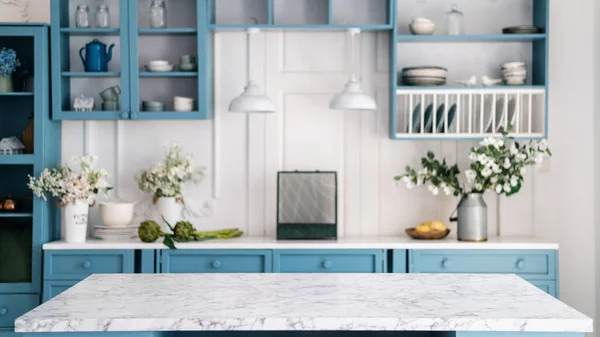 Empty marble kitchen island with clean surface in blue vintage kinchen in provence style. Dining table against blurred stylish furniture with drawers and kitchenware. Pendant lights hanging above.