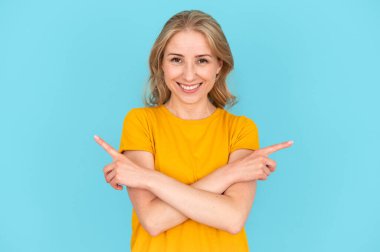 Mutlu kadın ellerini çapraz yaptı, işaret parmağıyla işaret etti, farklı teklifler sundu, çözümler önerdi, ürünleri karşılaştırdı. Gülümseyen kadın mavi fotokopi arkaplanındaki kameraya bakıyor.
