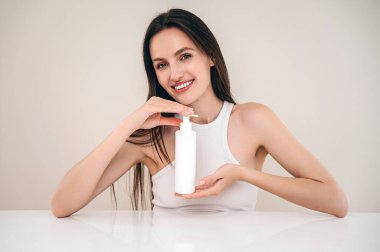 Elinde kozmetik şişeyle gülümseyen kadının portresi. Cilt bakımı ve kaplıca için organik ve doğal ürünler. Şımartma ve su verme konsepti. Boşluk arkaplanı kopyala