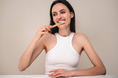 Mutlu kadın bambu diş fırçası kullanarak dişlerini fırçalıyor. Reklam konsepti ağız temizliği ve diş bakımı. Işık kopyalama alanı arka planına karşı model