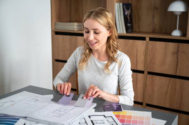 Yaratıcı insanların çalıştığı yer. Yeni bir proje üzerinde çalışan iç mimar, yenilenmiş evdeki duvarları boyamak için renk paletini seçiyor. Gülümseyen kadın yenilenmiş ev için malzemeleri birleştiriyor