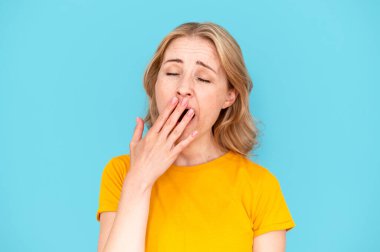 Tired woman with closed eyes yawning and covering mouth with hand over blue studio background. Feeling bored and sleep. Lack of energy concept. Need some relaxation clipart