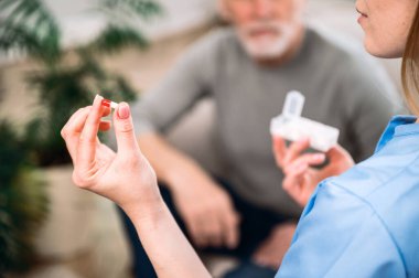 Doktorun elindeki tıbbi haplara odaklan. Hemşire orta yaşlı bir adama ilaç gösteriyor. Evde tedavi görmesi gerektiğini açıkla. Ağrı kesici, sakinleştirici ya da antibiyotik reçetesi