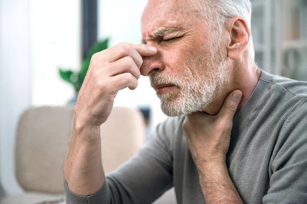 stock image mature man with virus symptoms, feeling unwell and touching nose bridge. male with nasal discomfort, headache suffer and acute pain in throat. health problem and medicare concept.