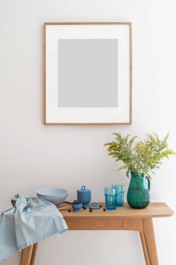 Duvardaki ön manzara çerçevedeki ahşap masa vazoda çiçekler, temiz bardaklar ve tabaklar, kapaklı ve taze yaban mersinli seramik yiyecek kabı