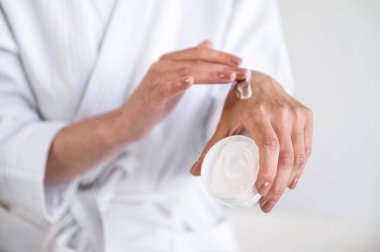 Beyaz paketli yumuşak desenli şımartıcı krem taşıyan kadınlara odaklan. Kadın tenine dokunuyor ve doğal kozmetik ürünler uyguluyor..