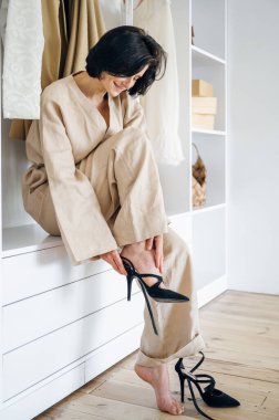 Giysiler için açık depo kavramı. Kadınlar parti için giyinir, yüksek tepelere çıkar, şık kıyafetlerle garsoniyerin yanında otururlar. Evdeki oda çok düzenli..