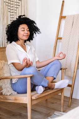 Huzurlu Afro-Amerikan kadın evde meditasyon yaparken Lotus pozu veriyor. Refah ve stres rahatlama kavramı