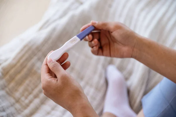 Close-up of afro american woman holding pregnancy test in hands. Checking and waiting positive or negative results. Artificial insemination. Infertility problem. Hope concepts