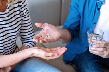 Orta yaşlı adam kadınlara tablet veriyor. İçmek için bir bardak su tutuyorum. Evde hap ve vitamin alıyordum. Tıp, sağlık hizmeti konsepti. İlişkide yardım ve varsayım