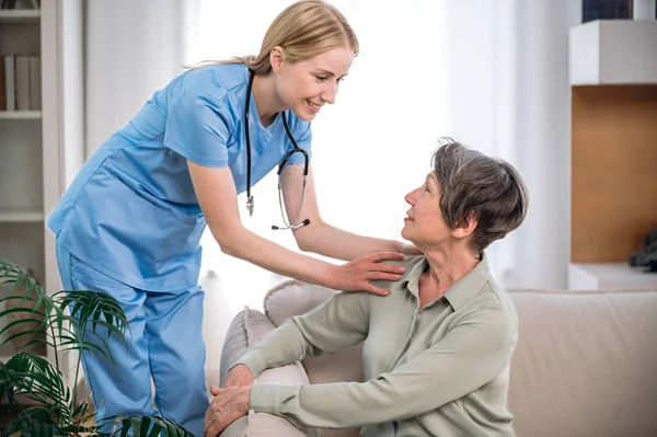 Support and medical care at home. Smiling professional physician or nurse touching shoulders of senior female at appointment. Doctor visiting and consulting patient