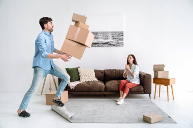 Karton kutular taşınma sırasında erkeklerin elinden yeni konaklama yerlerinde düşer. Genç yetişkin bir adam endişeli surat yapıyor. Kadın sarkık karton yığınına bakıyor.