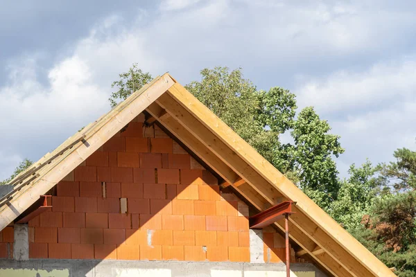 Waterproof layers on gable truss roof top with boards and planks. Attic elements on new brick house with wooden rooftop in the process of construction against blue copy space sky on background