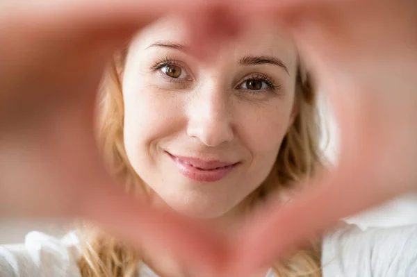 Close up portrait smiling happy woman making heart shape gesture. Like, love sign from fingers. Kindness, support concept. Expressing gratitude at camera on video call with clothes friends and family