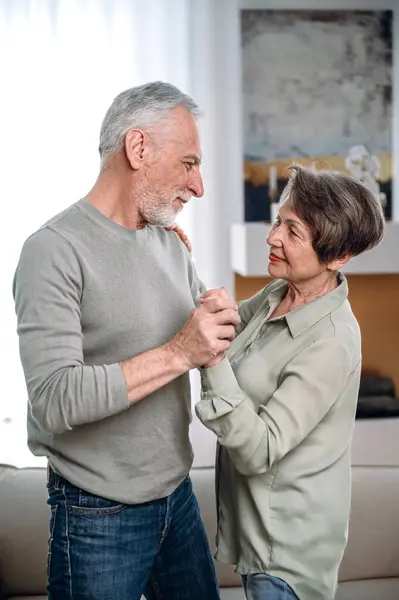 elderly loving couple dancing in living room relaxing at home on weekend together. understanding, affection, harmony between spouses. vertical shot with man and woman support each other in retired age