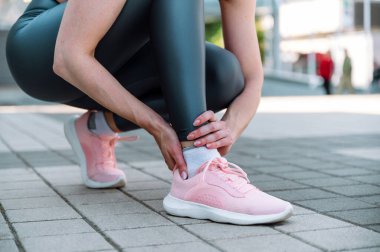 Ayak bileği ağrısı, spor sakatlığı. Spor ayakkabılı bir kadının acı dolu ayaklarıyla görüntüsü. Burkulma, gerilme, kırık, tendonit. Çalıştırıldıktan sonra sağlık sorunları kavramı.