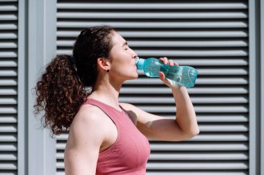 Koşu yaptıktan sonra plastik şişede su içen gözleri kapalı bir kadının profil portresi. Bayan sporcu spor sonrası dinleniyor..