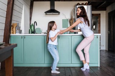 Gülümseyen genç anne, sevimli çocuğa modern mutfakta dans etmeyi öğretiyor. Konforlu evde iyi hafta sonları. Mutlu bir çocukluk. Birlikte boş zaman geçirmek..