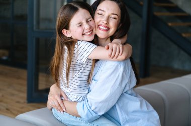 Mutlu aile ilişkileri konsepti. Güzel annesine sarılan gülümseyen çocuğun portresi. Kadın ve çocuk evdeki kanepede oturup oyun oynuyorlar..