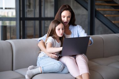 Mutlu kadın ve keyifli çocuk dizüstü bilgisayarda video izliyor oturma odasında rahat bir koltukta oturuyor, modern teknolojileri kullanıyor, hafta sonları evde eğlenerek vakit geçiriyorlar.