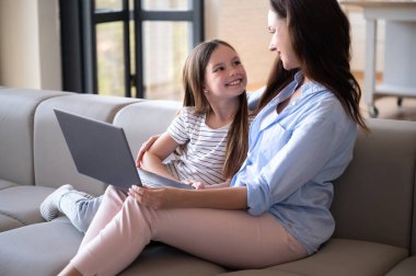 Kanepede oturup dizüstü bilgisayarda ilginç bir masal izlerken annesine gülümseyen kız. Neşeli kadın kızıyla vakit geçiriyor. Mutlu annelik kavramı