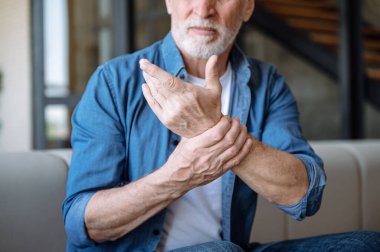 Cropped shot of unhappy middle aged man suffering from wrist pain, feeling numb and discomfort in hand. Elderly male has joint ache and inflammation. Arthritis treatment concept clipart