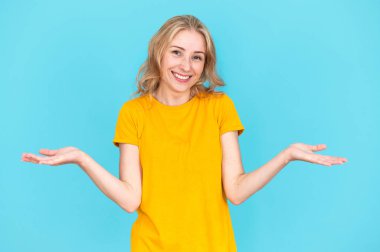 Seçim yapan genç bir kadın. Kameraya bakıp avuçlarını havada tutan gülümseyen bir kadın stüdyoda mavi arka planda. Alan reklam kavramını kopyala