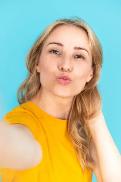 Taking duck face selfie. Self portrait of young smiling woman isolated on blue background. Making photo on cellphone or camera. Sharing positive emotions in social media. Create content
