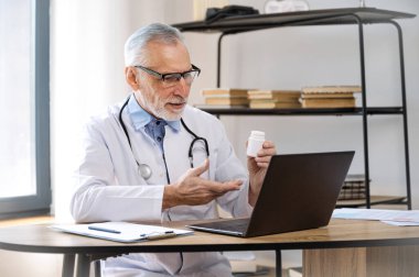 Üniformalı yetişkin bir doktor laptopp kullanıyor, görüntülü konuşma yapıyor, hastaya uzaktan danışmanlık yapıyor ve ilaç alması için tıbbi tavsiyelerde bulunuyor. Eczane reçetesi kavramı