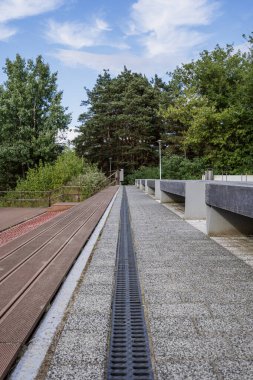 Şehir caddesinde beton kiremitli kaldırımda su boşaltma sisteminin metal ızgarası. Park yakınında dinlenmek için rahat bankları olan kamusal alan. Temiz patika ve açık alan