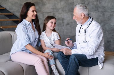 Mutlu gülümseyen kız, doktor randevusunda annesiyle oturma odasında oturuyor. Pediyatrist aileyi ziyaret edip tedavinin olumlu sonuçlarından bahsediyor. Tıp ve sağlık hizmetleri kavramı