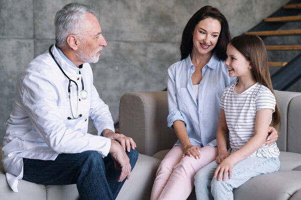 Счастливая молодая мама с маленькой дочкой имеют консультацию семейного врача-мужчины на дому. Педиатр разговаривает с пациентом во время визита. Концепция здравоохранения
