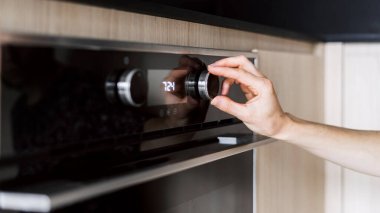 Kadın eli düğmesi kontrol panelinde mikrodalga modu olan modern fırında yemek pişirmek için program seçin. Kadın mutfak gereçlerinde yemek pişirmek için sıcaklığı ve zamanı seçer.