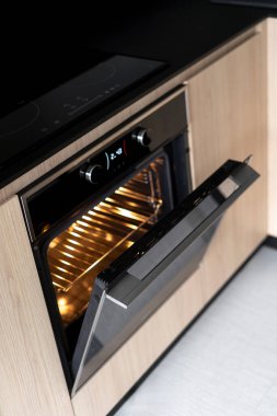 Cam seramik indüksiyon sobası açık kapılı elektrikli fırının üzerinde. Yüksek açılı görüntü ve donanım. Ev aletlerinin mutfak alanındaki dikey görüntüsü