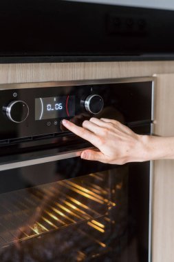 Ev aletleri, yemek pişirmek için mutfak malzemeleri. Modern elektrikli fırında dokunmatik ekrandaki kadın elle düğmeye basar, dikey çekim. Kadın kullanım kontrol paneli, mikrodalgada pişirme kipini seçin