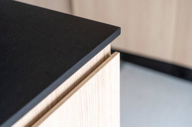 Siyah taş mutfak tezgahının detaylarını kapat. Modern apartmandaki ahşap dolabın üstündeki koyu gri masa yüzeyinin köşesi minimalist tarzda. Lüks evde İskandinav mobilyaları