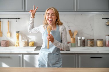 Mutlu kaygısız kadın, ailesi için sabah kahvaltısı hazırlarken modern mutfakta şarkı söyleyerek ve dans ederek eğleniyor. Etkilenmiş kadınlar evde yemek hazırlarken tembellik haftasonunun tadını çıkarırlar.