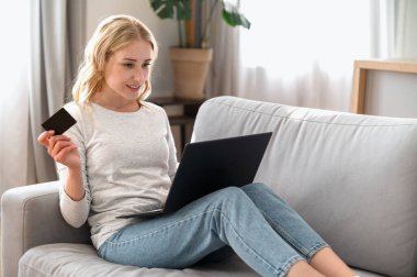 Kredi kartı tutan, dizüstü bilgisayar kullanan, faturaları internetten ödeyen mutlu bir kadın. Evde rahat bir koltukta oturan kadın güvenli bir internet ödemesi yapıyor, bilgisayardaki bilgi tarama bankacılığı hizmetine giriyor