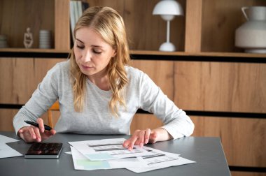 Meşgul kadın faturaları hesaplıyor, ev maliyesini ya da makinedeki vergileri kontrol ediyor. Kağıt belgelere bakan, ev bütçesini yöneten, aile harcamaları, gelir ve harcama parası odaklı bir kadın.