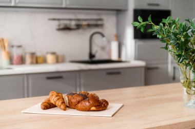 Ahşap mutfak adasında leziz taze ve ev yapımı hamur işine odaklan. Modern yemek odasının iç kısımlarında kahvaltıda lezzetli kruvasan bulunan bambu tepsisi. Kapalı alanda bulanık arkaplan