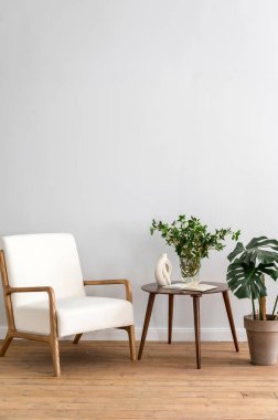 Konfor koltuğu ve yuvarlak sehpada ev dekorasyonu olan bir çatı katı. Yeni mobilyalar ve çiçek saksılarında yeşil bitkiler olan zarif oturma odasının dikey çekimi. Boşluk duvarını kopyala