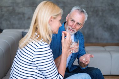 Karısına bakan orta yaşlı bir adam, ona ilaç hapı ve bir bardak su getirir. Hasta kadının antibiyotik tedavisi var. Sağlık hizmetleri kavramı.