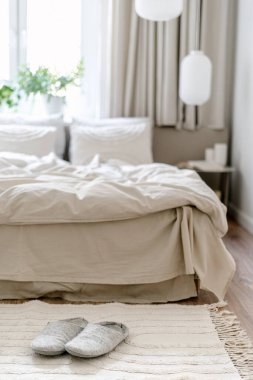 Yastıklı, battaniyeli ve çarşaflı halının yanındaki ev terliklerine odaklan. Işıl ışıl, İskandinav iç mekanı olan rahat bir yatak odası. Odada Hygge tarzı