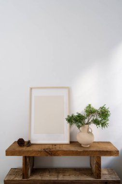 Ahşap banklı şık bir iç yapı çerçeve içinde maket resmi ve kopyalama alanı olan beyaz duvarlı yeşil bitki dallı seramik vazo. Tahtadan mobilyalar. İskandinav tarzı