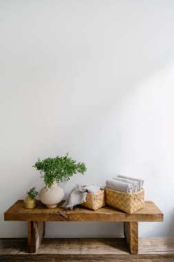 Katlanmış, taze, temiz, yumuşak ve kuru duş havlusu ve minimalist banyo içinde beyaz fotokopi duvarı ile yeşil dalı olan vazo. Ahşap bankta ev dekorunun dikey çekimi