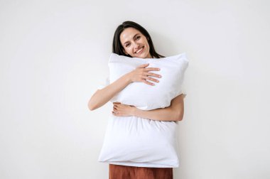 Güzel pijama giymiş neşeli bir kadının portresi. Yastığa sarılmış, beyaz fotokopi çekilen arka planda tek başına duruyor. Sağlıklı bir uykudan sonra iyi bir ruh hali. Evde mükemmel sabah kavramı