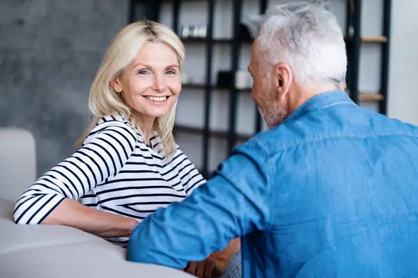 stock image Happy smiling woman sitting on couch at home and listen to husband. Mature family couple enjoy weekend, spending time together, speaking about life and sharing feelings