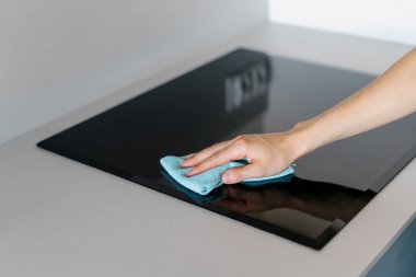 Mavi halıyı tutan ve siyah boş seramik sobayı temizleyen kadına odaklan. Modern mutfaktaki beyaz tezgahta entegre bir alet. Ev işleri..